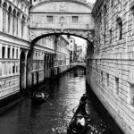 In 2019, I was in Venice (Italy) traveling with my parents and a group of friends. We were walking around the city and I saw the beauty of the place. The image shows two gondolas with couples strolling through the city and passing under the famous Bridge of Sighs, which connected a prison with the Palazzo Ducale. The bridge's name is based on a legend that the prisoners crossed the bridge, taking their last breath, as it would be the last time they would see the outside world.